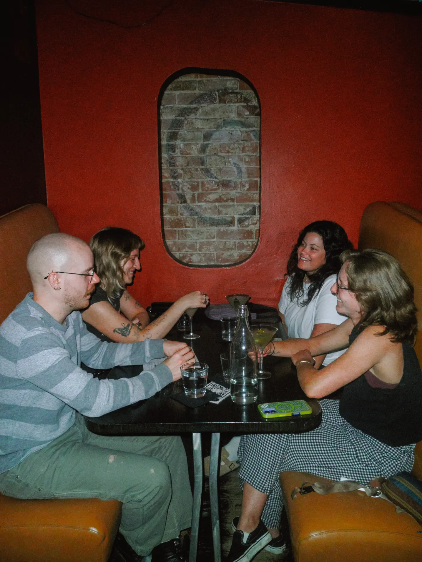 Four friends laughing in a booth against the red wall inside Elliot's