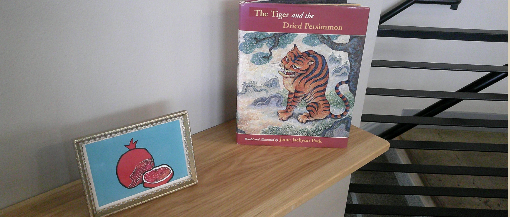 The Tiger and the Dried Persimmon book with a framed persimmon illustration on a shelf