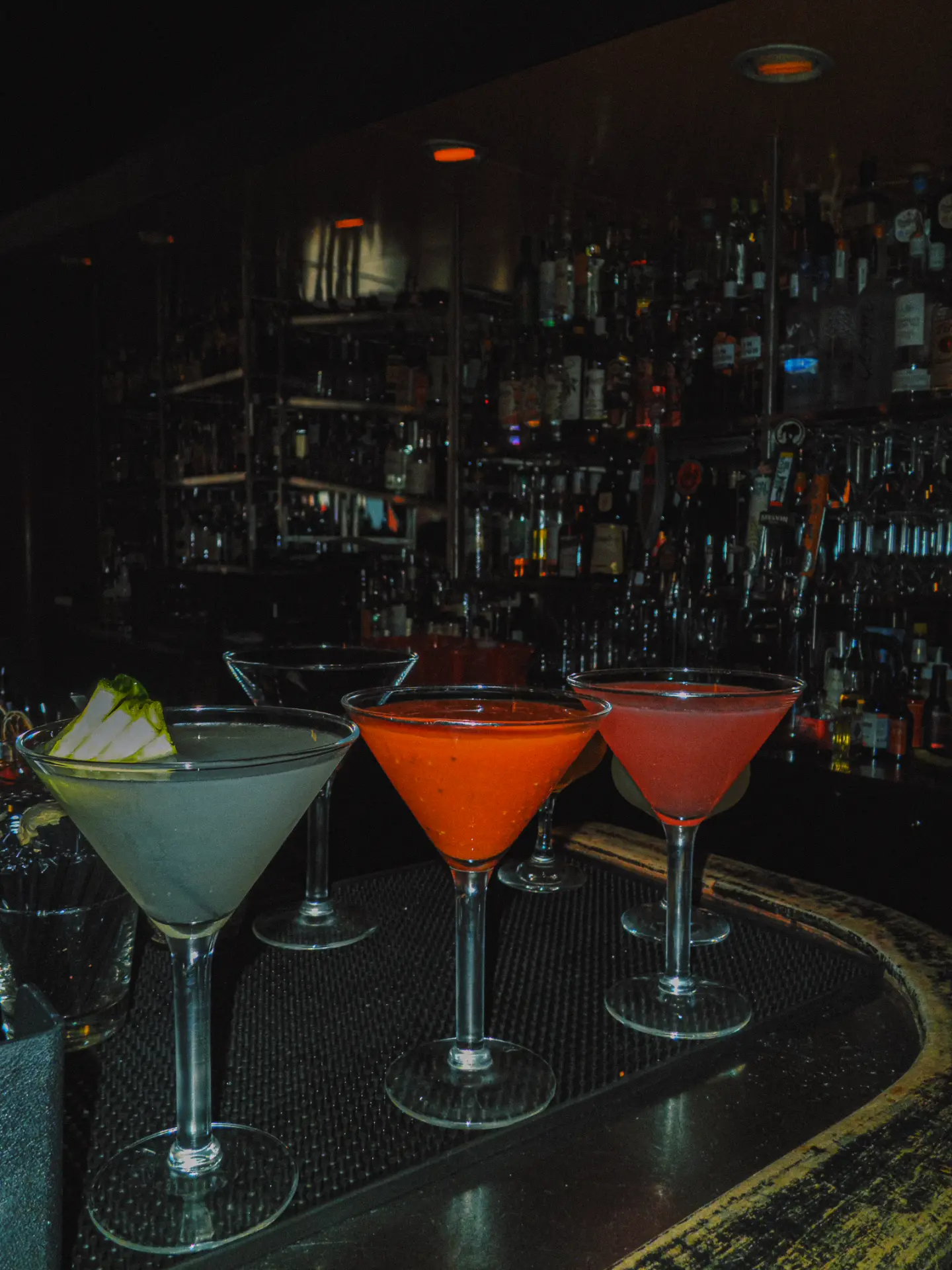 Three martinis lined up on the bar in front of the back bar bottles