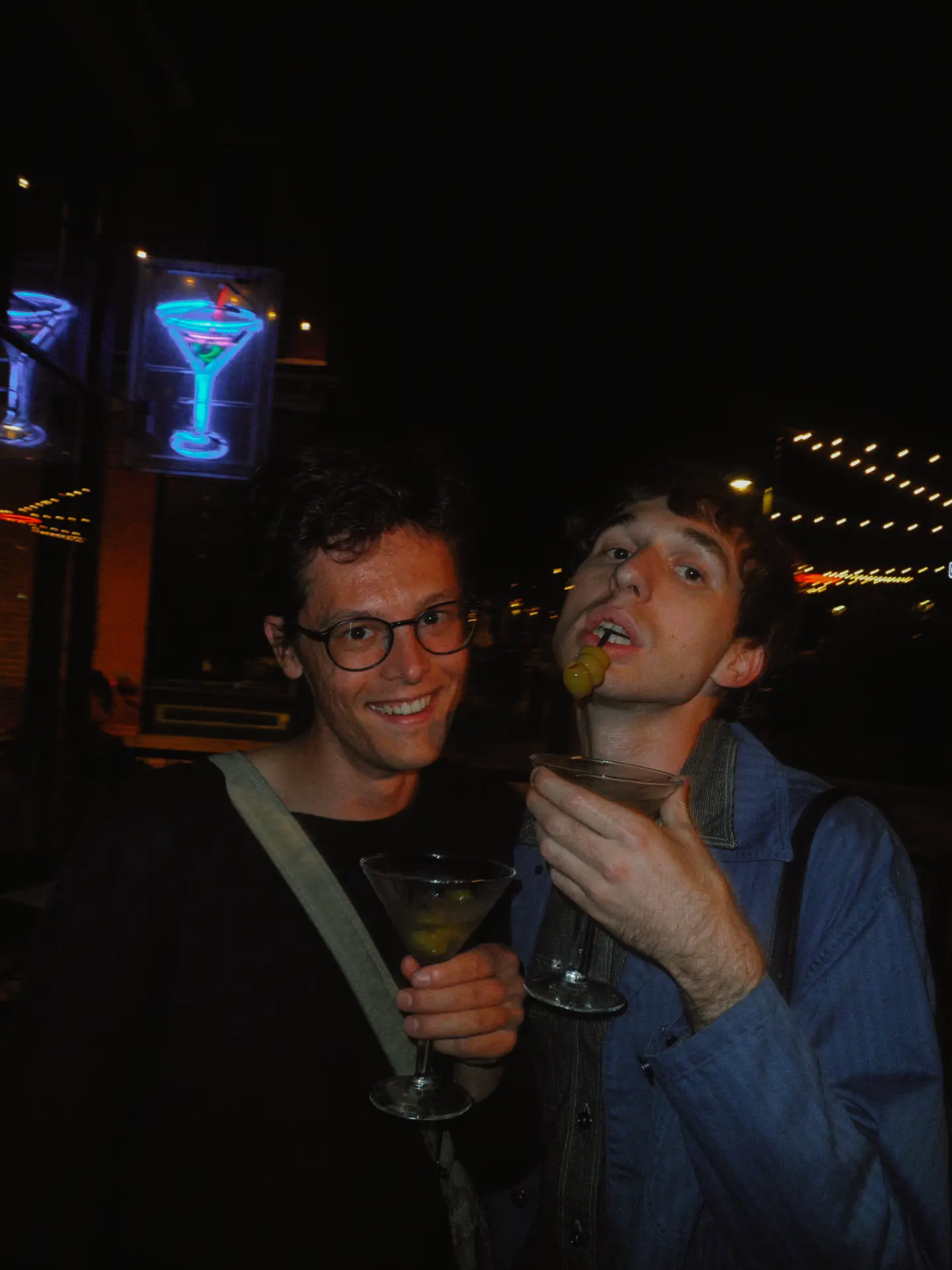 Two guests with martinis under the neon martini signs outside Elliot's
