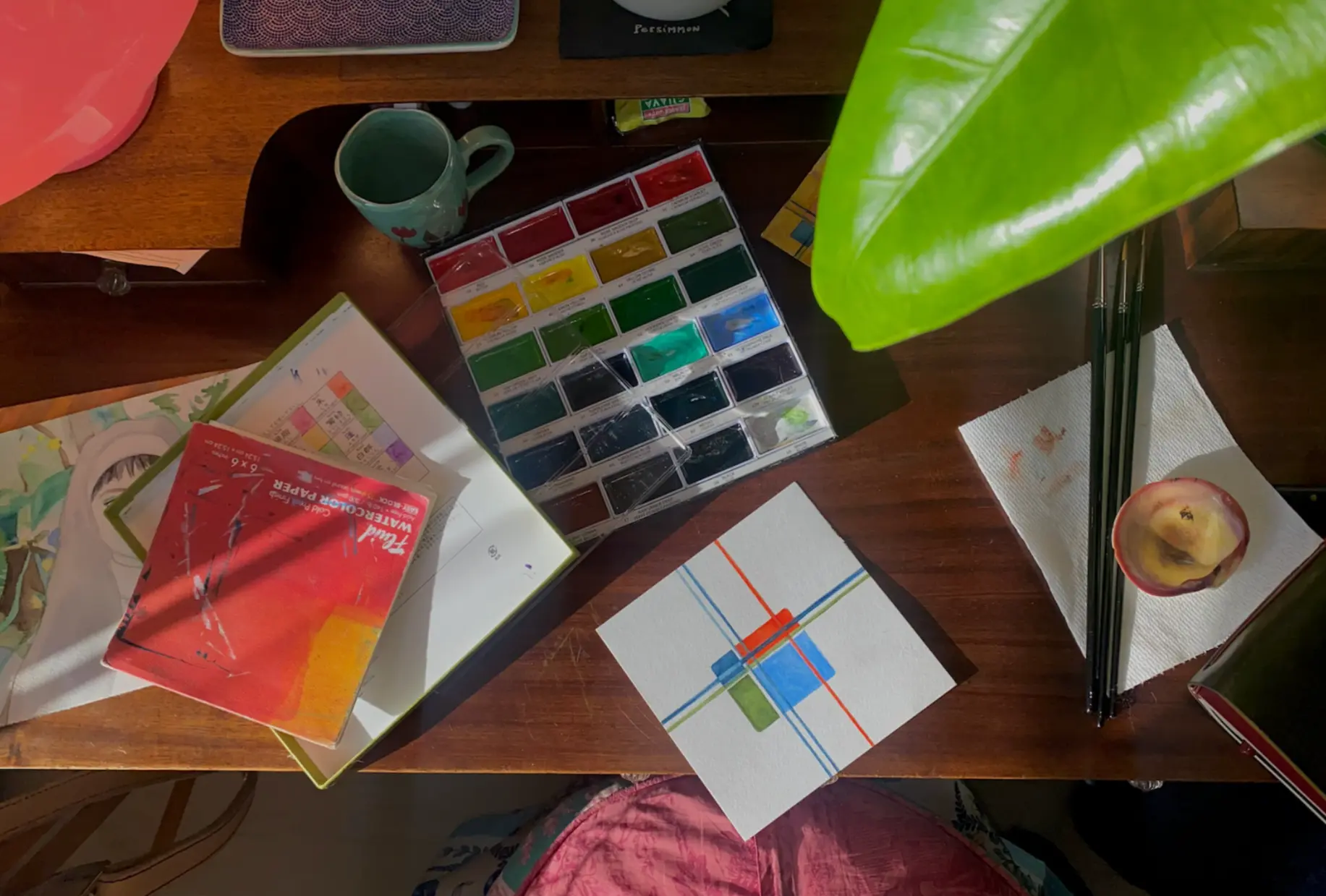 Overhead photo of Kalyana painting the AMLAMAKA mark in watercolor at her desk