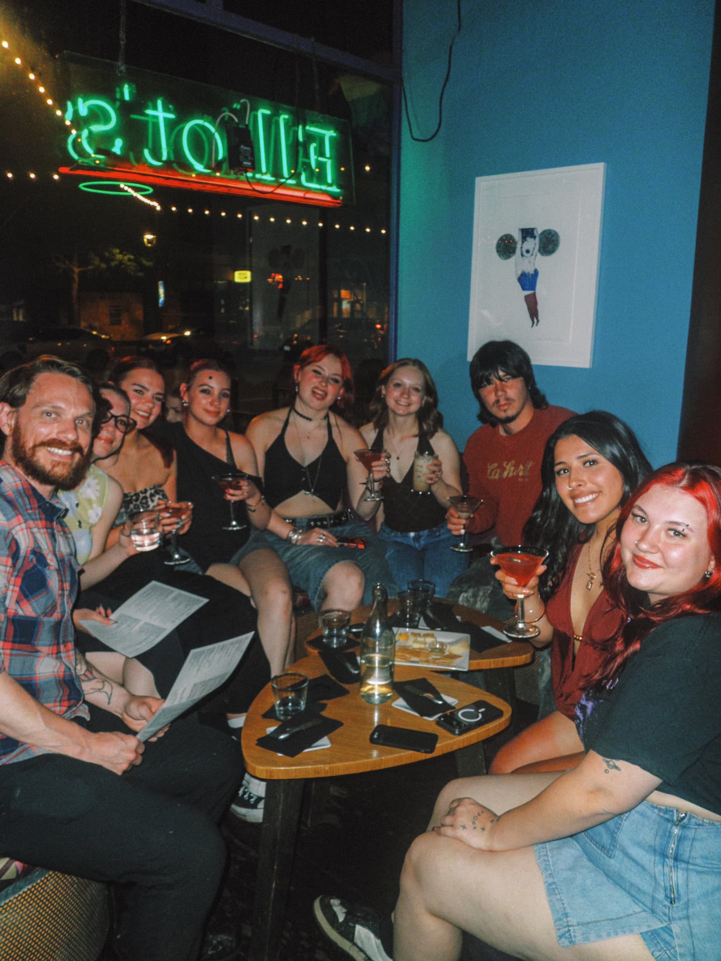 Large group of guests raising martinis under the neon Elliot's window sign